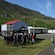 People gathered outside a silo like building between a hillside and a jetty